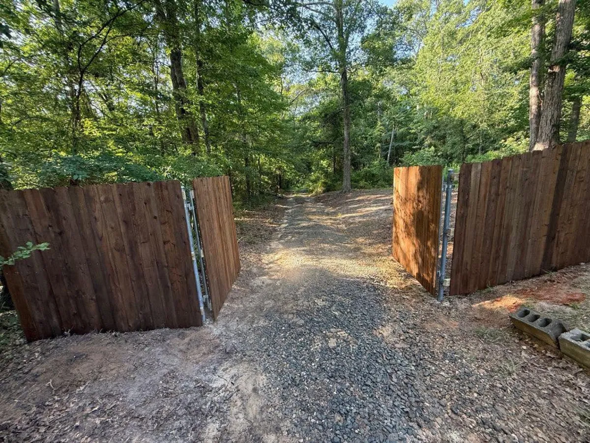 Stained wood privacy fence with double drive gate on a gravel drive